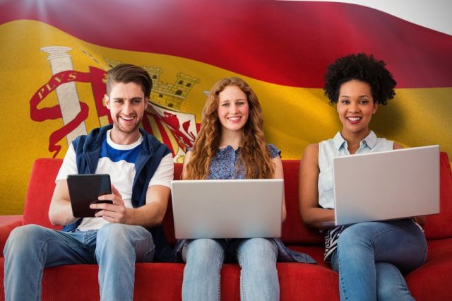 Students studying with laptops in front of Spanish flag