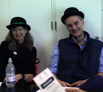 Two people wearing hats sitting at a table, smiling.