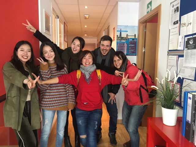Group of six people smiling and posing in a hallway.