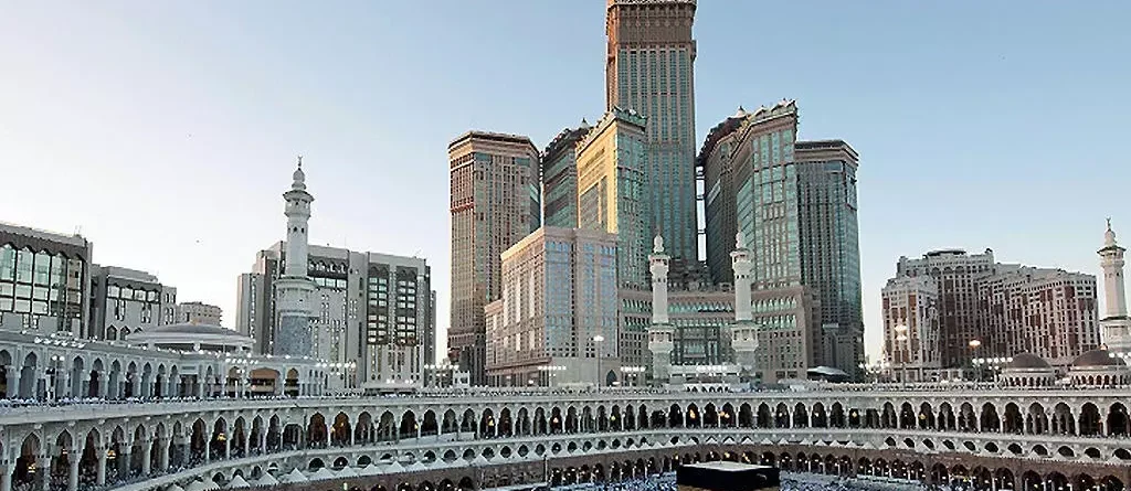 Kaaba surrounded by pilgrims in Mecca with Abraj Al Bait Towers in the background.