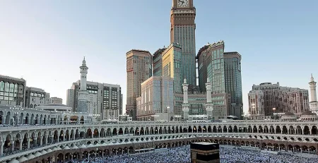 Kaaba surrounded by pilgrims in Mecca with Abraj Al Bait Towers in the background.