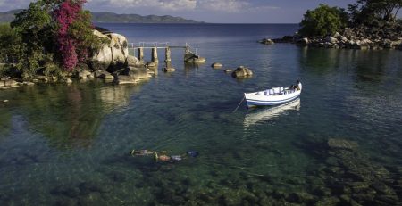 Scenic view of a clear lake with a boat and a swimmer near rocky shore.