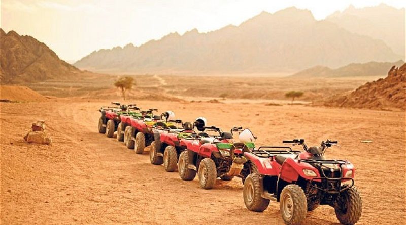 Row of ATVs in a desert landscape with mountains in the background.