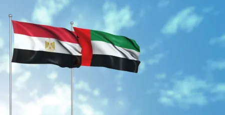 Egyptian and UAE flags waving against a blue sky.